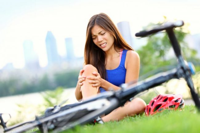 Young woman laying next to her bike holding her leg in pain