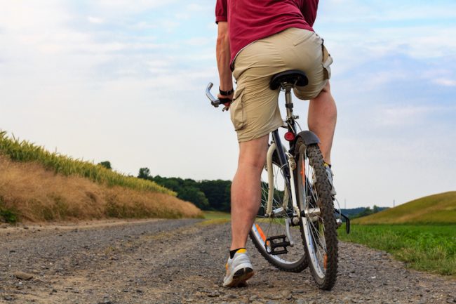 Common calf muscle injuries from cycling man stops on mountain bike on a country lane