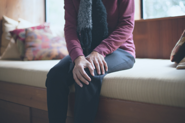 Older woman on sofa holding knee joint in pain