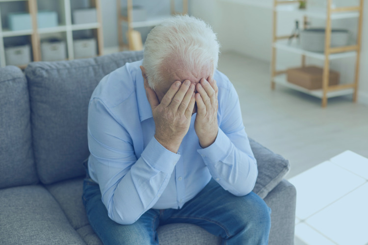 Man sat on sofa with hands over his face