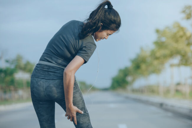 Young woman in sports wear holding her hamstring in pain