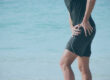 Sporty man on beach holding hip in pain