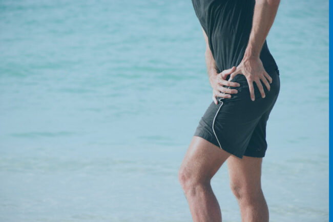 Sporty man on beach holding hip in pain