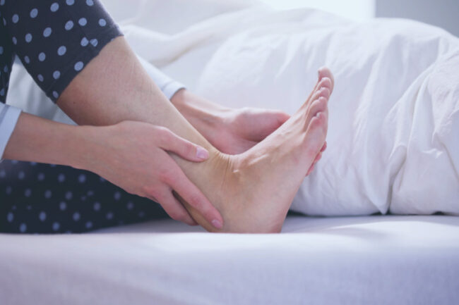Woman holding her heel and foot in bed