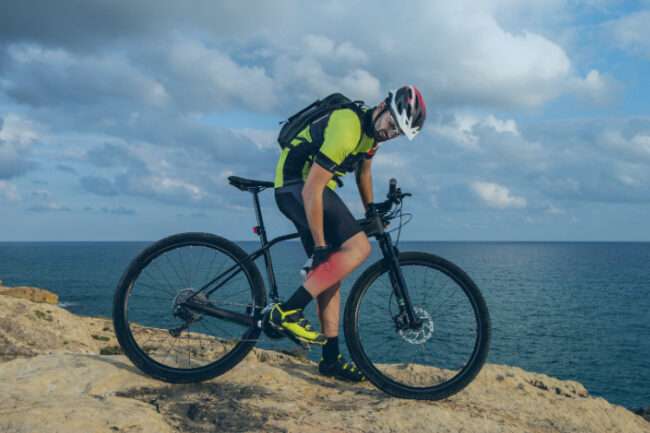 Man on bike holding burning calf muscle in pain
