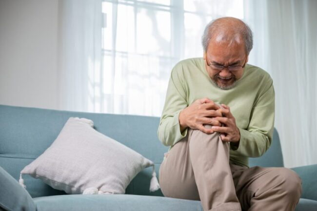 Older man on sofa holding his knee in pain