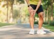 Man running and holding knee in pain, with sun shining through trees