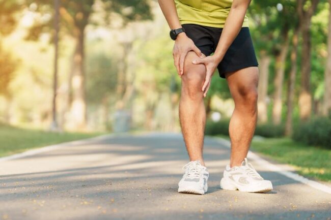 Man running and holding knee in pain, with sun shining through trees
