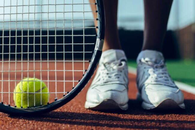 Tennis ball and racket with tennis players feet on the court