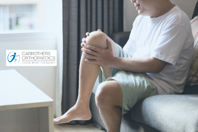 Man holding knee in pain sitting on sofa