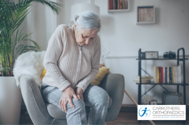 Older woman at home with jumper and blanket, holding knee in pain