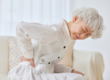 Older woman sat on sofa holding hip in pain