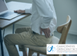 Man sat at desk holding his hip in pain