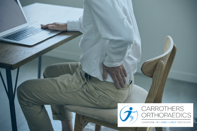 Looking to Relieve Joint Pain Man sat at desk holding his hip in pain