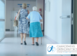 Older woman leaving hospital with a walking stick and family member